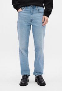 Heled sinised denim püksid otse lõikega, esipocketsite ja vööloopidega, kombineeritud mustade libisevate kingadega.