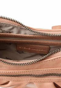Interno di una borsa sintetica rosa chiaro con chiusura a zip. Presenta una fodera con motivo e un'etichetta marrone cucita all'interno.