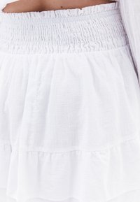 Falda blanca con volantes y cintura fruncida, que presenta una tela ligera y texturizada con un diseño de volantes. Ajuste regulable mediante elástico.