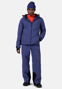 Fioletowa kurtka ocieplana z zamkiem błyskawicznym z przodu, z odpinanym kapturem, zestawiona z pasującymi fioletowymi spodniami i czarnymi akcentami na mankietach.