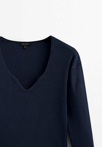 Mörkblå ribbad tröja med V-ringning och långa ärmar, med en mjuk textur. Etikett synlig vid ringningen.