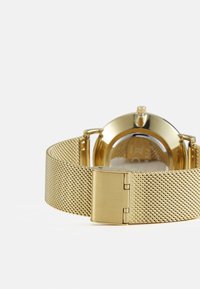 Bracelet de montre en maille dorée avec un boîtier rond. Présente une boucle en métal poli et une surface lisse et réfléchissante. Design minimaliste sans marquages visibles.
