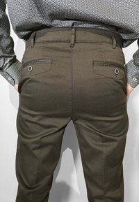 Pantaloni kaki con motivo strutturato, dotati di due tasche posteriori e un bottone decorativo. Abbinati a una camicia a motivo nero e bianco.