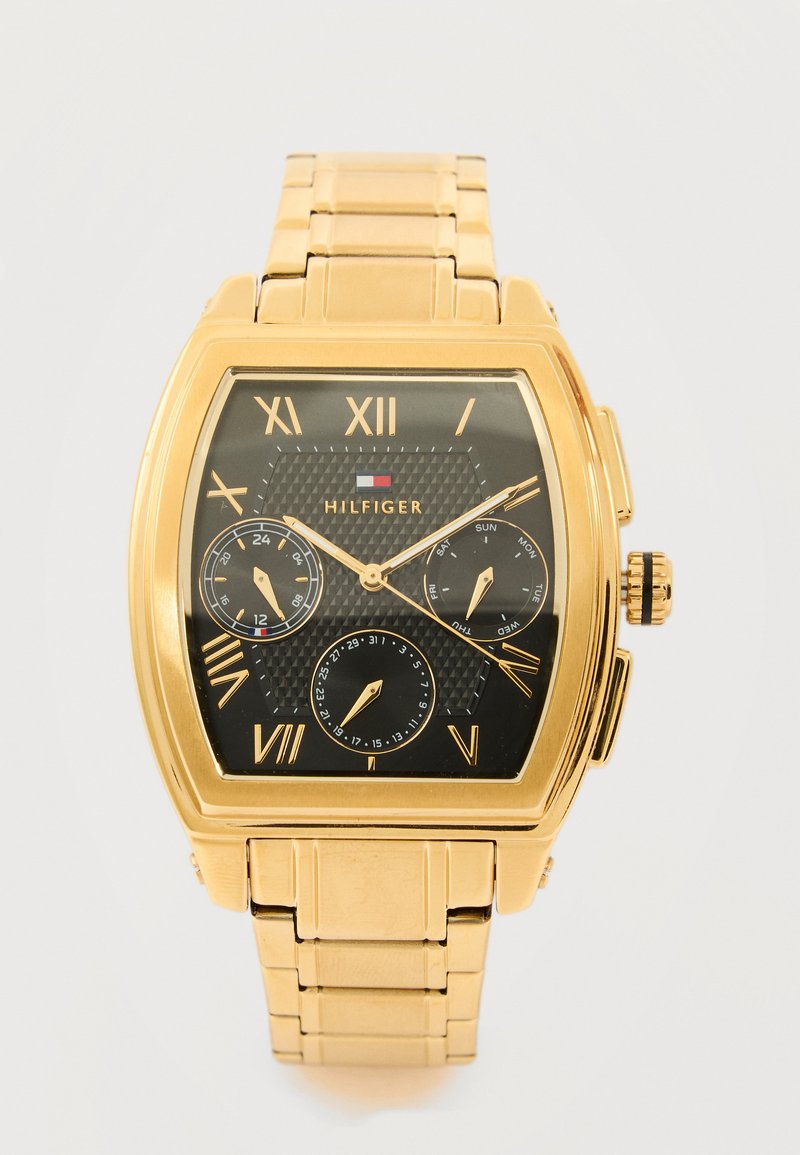 Orologio da polso quadrato in tono oro con quadrante nero, numeri romani, tre quadranti secondari per 24 ore, giorno e data, e marchio "Hilfiger".