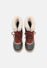 Brune snøreboter med en fluffy hvit foring, grå gummibase, rund tå og horisontale sømdetaljer på overdelen.