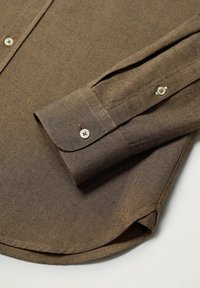 Bruine katoen shirt met een afgeronde zoom, knoopmanchetten en een subtiel textuurpatroon. De knopen zijn wit met een enkele opening voor bevestiging.