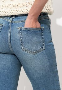 Jean en denim bleu clair au design ajusté, avec deux poches arrière et une légère élasticité. Le tissu a une texture lisse et des détails de couture subtils.