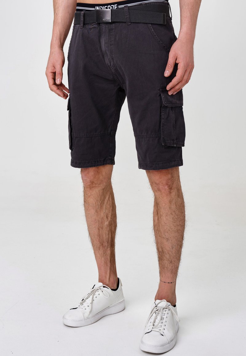 Schwarze Cargo-Shorts aus Baumwolle mit mehreren Seiten Taschen, einem entspannten Schnitt und einem genähten Saum, kombiniert mit weißen Turnschuhen.