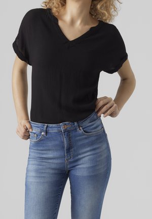 Haut noir à manches courtes avec un col en V, associé à un jean bleu ajusté avec une texture délavée et un design classique à cinq poches.