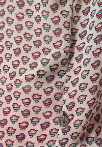 Blusa in tessuto leggero di un rosa pallido con un motivo floreale ripetuto in rosso, verde e blu. Include un'etichetta circolare del marchio in argento.