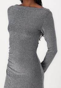 Abito grigio a maniche lunghe con una texture scintillante, caratterizzato da un scollo off-the-shoulder e una silhouette aderente. Tessuto liscio con una leggera lucentezza.