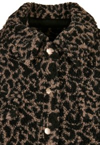 Manteau texturé noir et beige avec un motif, doté d'un col à revers et de boutons métalliques pour la fermeture. Tissu épais et moelleux.