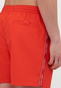 Pantaloni scurți de baie roșii, dintr-un material ușor, cu o talie elastică, o buzunar la spate și accente laterale cu logo-ul Calvin Klein.