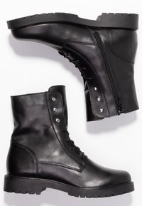 Bottines en cuir noir avec un bout arrondi, un laçage à l'avant, une fermeture éclair sur le côté et une semelle en caoutchouc texturée avec un motif de semelle robuste.