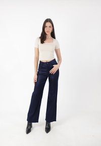 Beżowy dopasowany top z krótkimi rękawami, połączony z granatowymi spodniami o szerokich nogawkach z wysokim stanem, z delikatnym połyskiem. Czarne szpilki za kostkę.