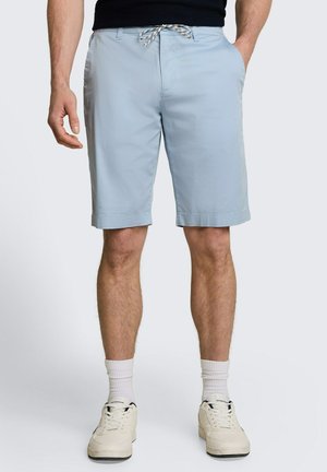 Mann trägt hellblaue Shorts mit Kordelzug, weiße Kniestrümpfe und weiße Sneakers, steht mit entspannt seitlich hängenden Händen.