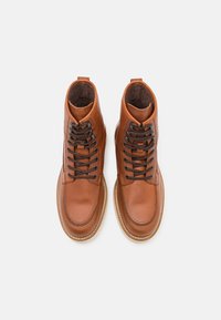 Brown leather ankle boots with black laces, rounded toe, and textured detailing. Features padded collar and contrasting rubber sole.