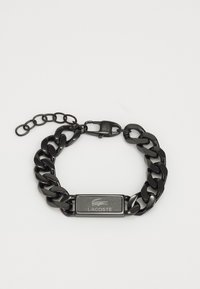 Pulsera de cadena negra con una placa metálica rectangular grabada con el logotipo. Incluye un cierre de langosta y una cadena de eslabones ajustable.