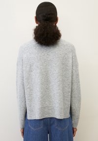 Maglione grigio chiaro a maglia con una vestibilità rilassata, spalle cadenti, orlo a coste e una texture morbida, abbinato a jeans in denim blu.