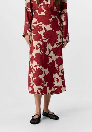 Floral midi skirt in beige with large red flower pattern, textured fabric, complemented by black mesh flats with crossed straps.