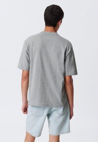 Gray short-sleeve t-shirt with a crew neck, made from cotton blend fabric, displayed from the back, paired with light denim shorts.