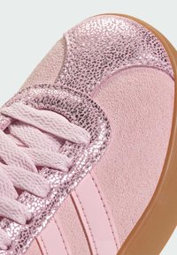 Pink suede sneaker featuring a sparkling glitter accent, lace detailing, and a textured rubber sole with pink stripes along the side.