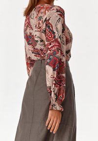 Blouse à manches longues avec un motif paisley en rouge, bleu et beige sur un tissu doux ; associée à une jupe grise jusqu'au genou.