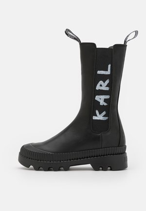 Stivale alla caviglia impermeabile nero con pannelli elastici laterali, suola in gomma texturizzata e dettaglio del logo bianco "KARL". Finitura in pelle liscia.