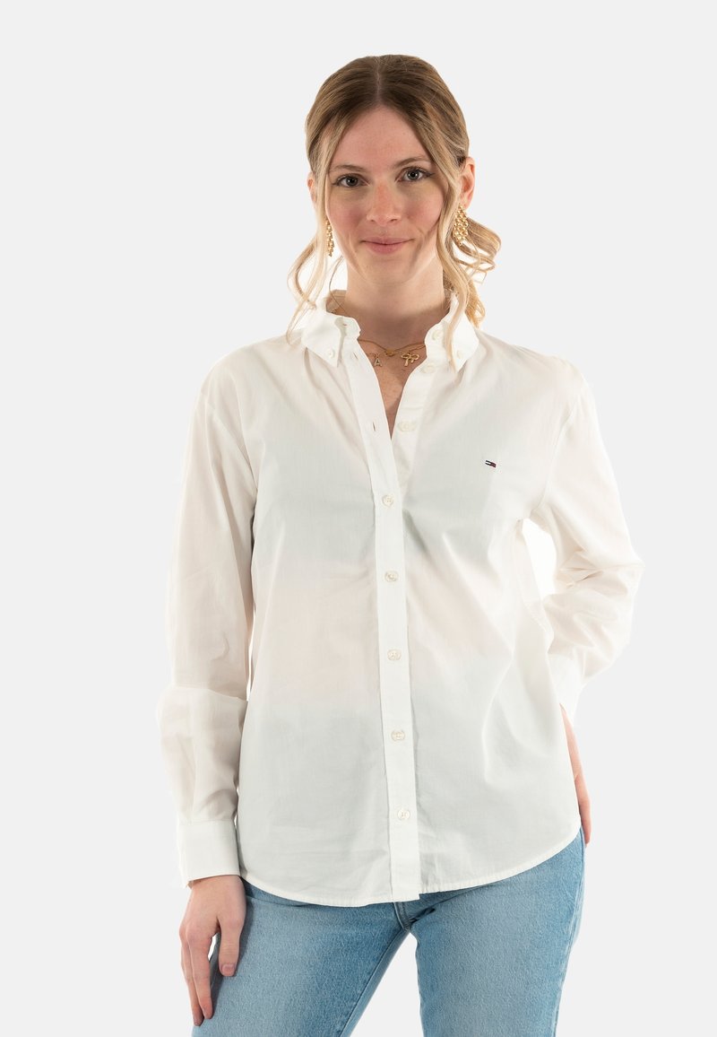 Camicia bianca con bottoni realizzata in un tessuto leggero, con colletto classico, maniche lunghe e un piccolo logo sul petto.