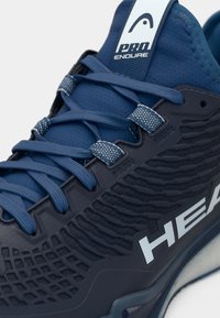 Modrá športová obuv s textúrovaným syntetickým zvrškom, plochými šnúrkami, spevnenými priechodkami a výrazným bielym logom na boku. Ľahký dizajn.