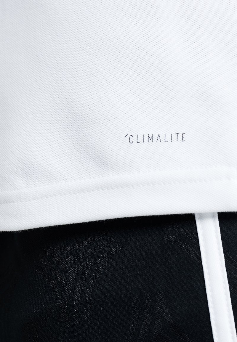 Tissu blanc avec le texte "Climalite" près du bord au-dessus d'un tissu noir avec un motif texturé subtil et une bande verticale blanche.