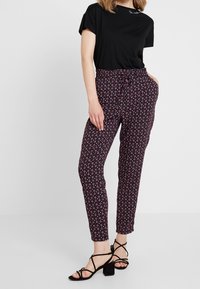 Černé tričko s krátkými rukávy ve spojení s úzkými kalhotami s vzorem v tmavě růžové a bílé barvě. Černé sandály na podpatku se pásky doplňují vzhled.