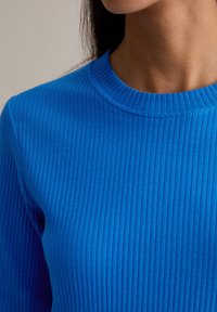 Niebieski prążkowany sweter z okrągłym dekoltem, prezentujący teksturowaną tkaninę i dopasowany krój. Bez wyróżniających się akcentów ani wzorów.