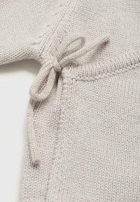 Lichtgrijze gebreide stof met een strikdetail aan de rand, die fijne getextureerde steken en ribbelafwerking toont.