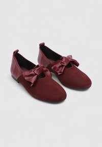 Zapatos de ante burdeos con detalles de cuero, puntera redondeada y un prominente lazo en la parte delantera. Suela plana y acabado interior suave.