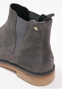 Bottine Chelsea en daim gris foncé avec panneau latéral élastique, languette, emblème métallique marqué et semelle crêpe marron clair.