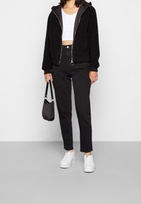 Czarna puszysta kurtka rozpinana na zamek, z kapturem, biały krótki top, czarne spodnie z wysokim stanem oraz białe trampki. Czarna torebka z krótkim paskiem.