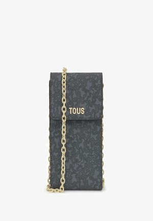 Bolso negro texturizado con cadena dorada y solapa plegable, que presenta el logo "TOUS" en dorado en la parte frontal.
