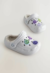 Weiße Clogs verfügen über ein weiches Futter, mehrere Belüftungsöffnungen und bunte Verzierungen in Form von Smileys in Lila, Grün und Blau.