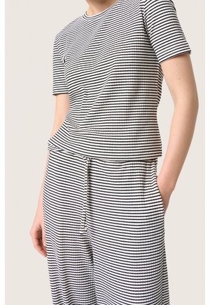 Person wearing a ribbed black-and-white horizontal striped short-sleeve top and matching drawstring pants, one hand in pocket.