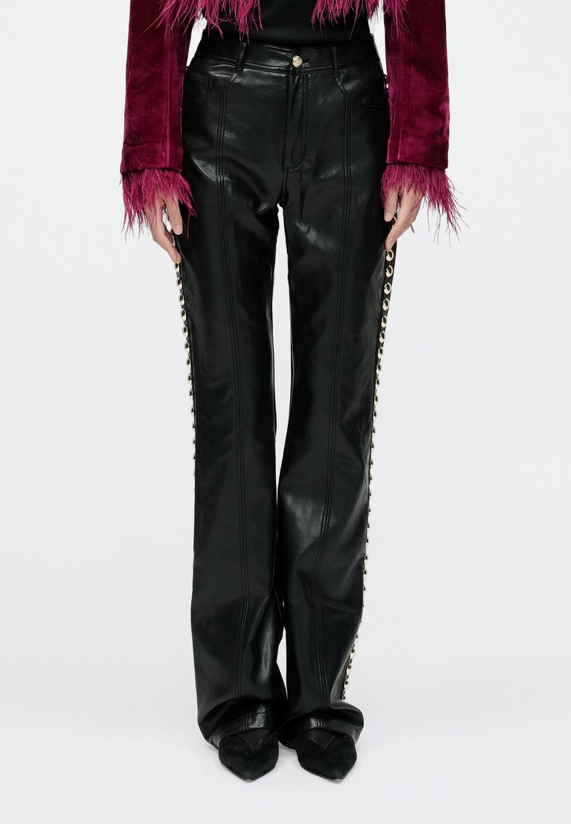 Czarne skórzane spodnie o prostym kroju nogawek, z akcentami w postaci złotych elementów ozdobnych wzdłuż bocznych szwów oraz gładką, błyszczącą fakturą.