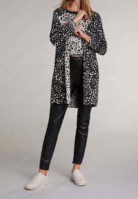 Czarny i biały sweter w printy noszony na wzorzystym topie, w połączeniu z czarnymi skórzanymi spodniami i białymi trampkami. Miękka tekstura i luźny krój.