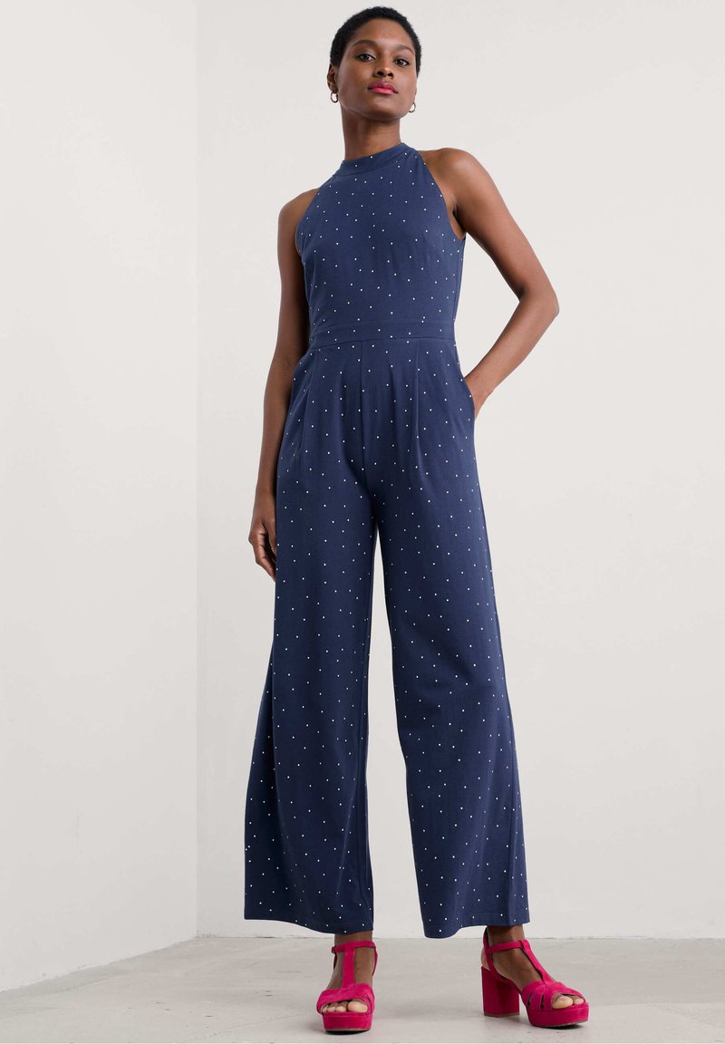 Tume sinine hüppeülikond valgete täppidega, ilma varrukateta, laiad jalad ja küljetaskud, koos erksate roosade platvormisaljadega.