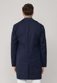 Cappotto trench navy con taglio dritto, maniche lunghe e colletto semplice. Presenta un design pulito sul retro senza hardware o dettagli visibili.