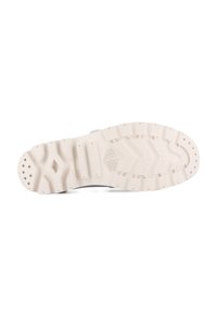 Suela de un zapato Palladium de color claro con profundos grabados, agujeros circulares en las zonas del talón y los dedos, y el nombre de la marca embosado en el centro.