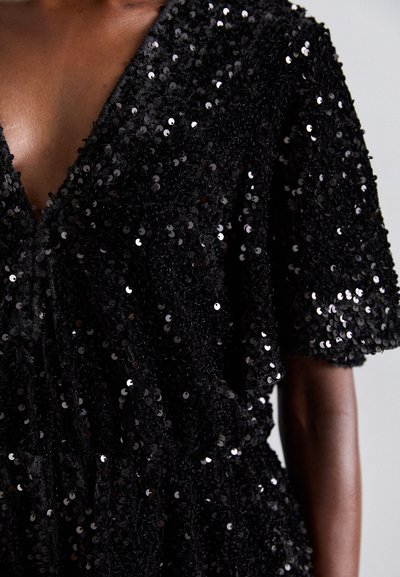 Schwarzes, mit Pailletten besetztes, strukturiertes Wickelkleid mit kurzen Ärmeln, getragen von einer dunkelhäutigen Person, die Oberkörper und Arm vor einem neutralen Hintergrund zeigt.