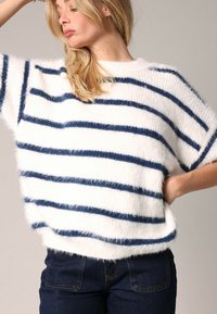 Pull blanc duveteux avec des rayures horizontales bleu marine, manches courtes et un col rond. Stylé avec un jean en denim foncé.