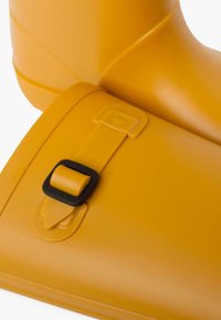Botín de lluvia de goma amarillo con un acabado brillante, que presenta una correa ajustable negra con un detalle de hebilla rectangular.