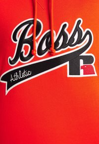 Sweat à capuche orange vif avec logo "Boss Athletic" en noir et blanc et lettre stylisée "R" rouge et blanche près du bas à droite du design.