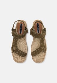 Brune semskede sandaler med runde utskjæringer, justerbar stropp og vevd jute-såler, med flat design og teksturert overflate.